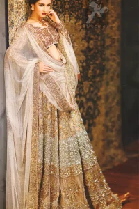 Ivory white and fawn bridal dress for the Walima function.Fully embroidered full-sleeved blouse. Lehenga features stunning embellishments. An embellished border is implemented on four sides of the dupatta. Crystal stones are crafted all over the dupatta. Ivory White Fawn Bridal Blouse And Lehenga.