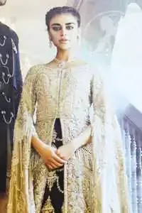 An ivory front open tissue shirt with heavy embroidery decorated with dull golden and champagne kora, dabka, tilla, naqshi, sequins and swarovski. It is further allured with cutwork and floral embroidery. Its umbrella sleeves is embellished with delicate zari work. Its black inner shirt is also embroidered. This outfit is artistically coordinated with black chiffon sharara which is allured with floral embroidery. This outfit is fully scalloped and enhanced by a thick floral embellished pattern. Dress comes with ivory dupatta which has finished edges and having sprinkled sequins pattern all over it.