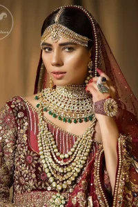This maroon angrakha frock heavily embellished in the front with silver gold kora dabka, kundan and stones work. One side shoulder neckline is beautifully ornamented with sequins lines in geometric manner. Paired up with matching brocade sharara which looks so magnificent. This outfit is meticulously coordinated with maroon dupatta with embellished borders on lengths.
