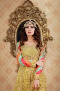 This outfit is decorated with antique shaded embroidery. The dress is fully embellished. Sleeves are decorated with different colour applique which adds to the look. It is adorned with thick embellished appliqued borders. It comes with yellow sharara and sequins spray all over it . It is coordinated with orange raw silk heavy embellished dupatta which has embellished with pink appliqued borders and beautiful tassels.