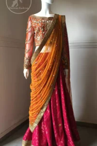 This dress is beautifully sculptured with floral embroidery. It is adorned with intricate detailing embellishment with antique gold kora dabka, tilla, kundan and swarovski. The blouse has full length sleeves decorated with floral motifs. It is coordinated with hot pink banarsi lenhengha finished with golden gota lace at the bottom. It is enhanced with floral motifs. The outfit is beautifully coordinated with orange pallu style dupatta embellished with golden Gotta lace on all sides.