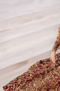 The grand maroon bridal stands out due to its uniqueness and the perfect fusion of modern cut and traditional embroidery. This halter neckline maxi is done with heavy embellishment of golden kora dabka, kundan, tilla, pearls and sequins work. It is further ornamented with detailed floral motifs. It is coordinated with brocade churidar pajama.