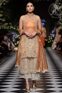 This outfit is stunningly perfect for any evening ensemble. It is paired with a sleeveless double layered shirt in organza fabric which is extensively hand worked in crystals and zardozi. This dress is beautifully sculptured with dull golden floral embroidery, adorned with cutwork borders embellished with tassels, kora, dabka, pearl and sequins work all over. It comes with embroidered trousers. It is coordinated with tissue dupatta which is furnished with four sided scalloped border.