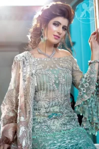 Boost your confidence and style in this glamorous off-shoulder short shirt in net fabric which is extensively worked in sequins and zerdozi work. It is further enhanced with scalloped sleeves and silver kora dabka work and sequins vertical lines all over. Paired up with heavily embroidered lehengha that gives the right amount of glamour to the outfit. It is finished with antique brass scalloped embellished border all around the dupatta.
