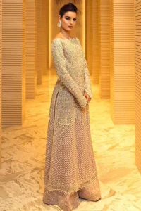 Boost your confidence and style in this glamorous attire accentuated with finest thread and zardosi work embroidery. This outfit paired up with salmon pink off shoulder long shirt embellished with thread embroidery and dull golden kora, dabka, sequins and tassels. It comes with beautifull sharara enhanced with floral motifs on the bottom. It is coordinated with chiffon dupatta which is sprinkled with sequins all over it.