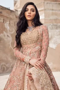 This garnet ensemble is sure to make you look like glamorous royalty with immaculate work covering every inch of the frock. The bodice of the frock is heavily embroidered with champagne zardozi work. Furthermore the hemline is ornamented with geometric patterns. It is coordinated with peach and light pink lehenga with a flowing train embellished with light golden and champagne embroidery and scattered floral motifs in a sequence.  this is an ensemble that deserves to be flaunted. Style it up with light pink dupatta having four sided embroidered border.