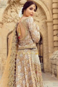 Strike a breathtakingly elegant pose in this wedding dress, designed with a beautiful blouse and a dramatic train. This artisan piece includes intricate hand-embellishment. This highly skilled technique involves hand needle work to add beads, kora, dabka, tilla and sequins to the fabric, giving our garments a unique look. The blouse is also enhanced with tassels on the hemline and back is adorned with horse shie neckline. Zardozi work is done in the shades of golden and silver. Dupatta is decorated with sequins spray on the canvas and finished with embroidered border on four sides which makes this outfit more beautiful.