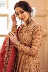 Chic and sophisticated perfectly describe this simply stunning wedding dress. This artisan piece includes intricate hand embellishment. This technique gives our garments a unique look, and helps to sustain a traditional craft carried out by skilled artisans across Asia. The short frock is fully embellished with zardozi work in the shades of golden and silver on tea rose canvas. Finished with dangling pearls on hemline. Compliment the look with coral back train lehenga exaggerated with embellished bottom and sprinkled floral bunches. The coral raw silk dupatta is emphasized with intricate embroidered borders.