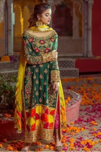 Beautifully elegant with a modern twist. This beautiful outfit comes with bottle green long shirt and colorful applique hemline, making an elegant, traditional and stylish mehndi dress. Excellence of craftsmanship is evident with intricate geometrical detailing that features the use of kora, dabka, crystals, sequins and glass beading. Furthermore it is enhanced with colorful floral motifs and golden zardozi work. It comprises with pink capri pants. Elegance is personified when it gets paired up with net dupatta with kiran on all sides and colorful strips on pallu.
