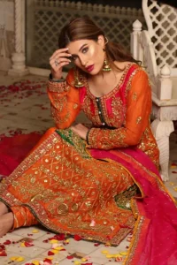 Get bold and beautiful with this uber-stylish ensemble that has flattering cuts, and a colour palette that is bewitching.  This orange long shirt adorned with intricate tilla work, kora, dabka and sequins is perfect ensemble for mehndi. Furthermore the shirt is also highlighted with pink embellished bodice and rest of the shirt is enhanced with geometric gota embroidery and green applique instantly draws attention.. It comprises with orange pajama adorned with gota work. Paired with pink chiffon dupatta with kiran lace finishing all around the edges that gives the right amount of glamour to the outfit.
