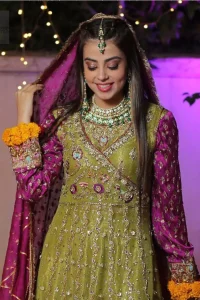 Nothing speaks of femininity and class louder than this mehndi outfits for bridesmaids. The sequinned whimsical florals embroidered across the flattering bodice in this ethereal frock is sure to turn heads in every room you walk into. The pairing of champagne zardozi work with parrot green fabric is an artist’s dream colour palette. The frock hemline is emphasized with banarsi applique details that gives perfect ending to this outfit. It comprises with matching tissue lehenga. The magenta organza dupatta with chann and gota work, finishing with kiran lace all around the edges makes the look complete. 