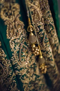 This artisanal piece is rendered in grace and timelessness. This outfit makes a statement in this stunningly floraison, perfect blend of glamour and tradition with outstanding craftsmanship and gorgeous detailing. This mehndi dress in a dreamy shade of green, enhanced with hand embellishments on neckline and sleeves. The wide flared lehenga is an example of remarkable handiwork with a lot of attention to detail. The sculptured embroidery is in the shade of golden. Complete the look with bottle green organza dupatta emphasized with tiny floral motifs on the ground and four sided embellished border.