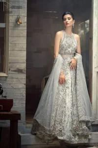 Nikah Wear - Light Grey Halter Neck Gown Lehenga. The floral and the flowery climber networks on fully embellished Halter neck and blouse has exquisitely exaggerated in the beauty of the costume making it very unique. The bottom lehenga with Fixed Waist Belt With Side Zip Closure is composed of Katan Banarsi Jamawar fully embellished with flowery climbers with Light Gray colour tone; being exquisitely beautiful in perfecting the complete outfit having a unique fabric and double flare lehenga that is in stellar combo with the blouse with finished edges and Dupatta sideways carried beautifully by the bride with organza fabric and Heavy beautiful golden and Grayish lace on all four bordered finished sides and dabka work on the net inside of the gorgeously made dupatta, whole this costume has its own unifying feature such as 100 % imported high quality overall highly embellished fabric making it the best choice to have by you on your big day.