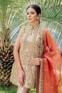 Envelop yourself into a dazzling love affair. The unique article in ivory colour just highlighted you at any event. The short shirt of the article is handsomely decorated with golden embroidery which includes kora, dabka, tilla, Kundan and Sitara work to make your event blazing and dazzling. It is enhanced with a collared neckline to make this outfit more formal when come with a sleeveless style. Further, it is coordinated with pant which is embellished with golden embroidery. Last but not least piece the dupatta comes in rust colour having four-sided embellished borders to encapsulate you in stars.