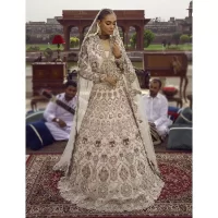 This vibrant canvas is all your brides need to cheer in at your special Nikah moments. A beige white blouse has a V shape neckline and full sleeves embellished with golden and silver embroidery. It is further intensified with special tills, dabka, kora, Kundan and the magic of zardozi to make your day outstanding and more funable. It is paired up with embroidered scalloped lehenga to fulfil the dreamy fairy look of the bride. Complete this article with a scalloped dupatta in the same colour with a four-sided embellished border and sequins sprayed all over to cheer up.