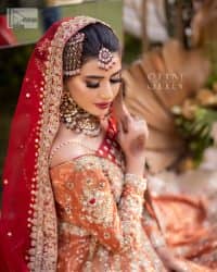 Shine bright in the sparkling ensemble from DeemasFashion. Introducing this reception outfit which begins with a rust pishwas.  This front en pishwas dipped in the richest shade of rust and is ornamented with golden embroidery which is further intensified with tilla, dabka, sequins and the real magic of zardozi. The strap neckline of the pishwas gives a unique aesthetic sense when comes with full sleeves. It is coordinated with an ivory lehenga whose border is embellished with golden embroidery. Finish this article with a dupatta framed with a four-sided embroidered border and sequin sprayed all over.