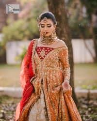 Shine bright in the sparkling ensemble from DeemasFashion. Introducing this reception outfit which begins with a rust pishwas.  This front en pishwas dipped in the richest shade of rust and is ornamented with golden embroidery which is further intensified with tilla, dabka, sequins and the real magic of zardozi. The strap neckline of the pishwas gives a unique aesthetic sense when comes with full sleeves. It is coordinated with an ivory lehenga whose border is embellished with golden embroidery. Finish this article with a dupatta framed with a four-sided embroidered border and sequin sprayed all over.