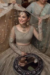 Regal and Charismatic - This is all the outfit is about! A desirable beige lehenga and choli are entirely heavily embroidered with silver colour and embellished with sequins, tilla, naqshi, Zardozi and Dabka. Its stunning heavily embellished blouse has full sleeves and the blouse consists of V shape neckline. It is coordinated with flared lehenga which is adorned with beautiful embroidery to make this walima wear balance. Finish this with a dupatta that has silver sequin and tiny floral motifs all over. The dupatta is framed with a four-sided embellished border to make this masterpiece unique and attractive.