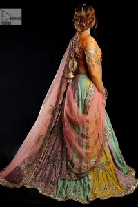 Fun colours, fresh you.  This breathtaking blouse in light orange colour is gracefully adorned with hand-crafted embellishments and lavish golden work creating a magnificent masterpiece to give you your desired appearance. The boat shape neckline of the mehndi wear is the epitome of beauty. Further, the embellished three-quarter is adorned with lavish designs and fine details making it a perfect choice to pair with the lehenga. It is organized with lehenga having multi-colour panels to give you a fresh and rainbow look on your mehndi. The lehenga is also adorned with tilla, dabka, kora, Kundan and the real magic of Zardozi. Complete this article with a dupatta, framed with four-sided borders and floral motifs on pallu to make your day Funday.