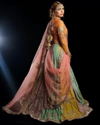 Fun colours, fresh you.  This breathtaking blouse in light orange colour is gracefully adorned with hand-crafted embellishments and lavish golden work creating a magnificent masterpiece to give you your desired appearance. The boat shape neckline of the mehndi wear is the epitome of beauty. Further, the embellished three-quarter is adorned with lavish designs and fine details making it a perfect choice to pair with the lehenga. It is organized with lehenga having multi-colour panels to give you a fresh and rainbow look on your mehndi. The lehenga is also adorned with tilla, dabka, kora, Kundan and the real magic of Zardozi. Complete this article with a dupatta, framed with four-sided borders and floral motifs on pallu to make your day Funday.