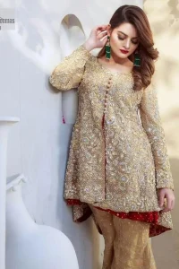Clean, modern and timeless. The beautiful front-open short shirt in a light golden colour is adorned with embellishments of silver embroidery. It is enhanced with tilla, dabka, kora, Kundan and the real magic of Zardozi. The round neckline makes this outfit unique and lovely. Further, the floral patterns on full sleeves also add super beauty to the outfit. The inner of the short shirt has a red frock combination that gives an aesthetic look. Complete this article with trousers in the same colour as a short shirt just to balance the royal look.   