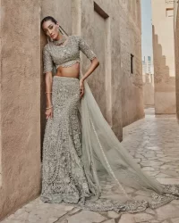 This fusion of floral embroidery is total fashion goodness for a walima outfit! A stunning teal grey organza choli embellished with intricate detailing finished with a scalloped border. The beautiful blouse is decorated with silver embellishment which is further prominent with tilla,daka, kora, Kundan and the real magic of Zardozi.  It is paired with a heavily embellished back-train lehenga with botanical motifs and geometric patterns. Its dupatta is made from a net. The dupatta is a wide embellished border that added divine charm to the entire ensemble.