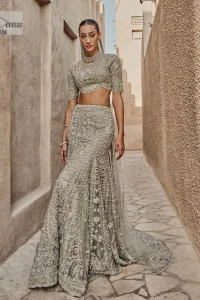 This fusion of floral embroidery is total fashion goodness for a walima outfit! A stunning teal grey organza choli embellished with intricate detailing finished with a scalloped border. The beautiful blouse is decorated with silver embellishment which is further prominent with tilla,daka, kora, Kundan and the real magic of Zardozi.  It is paired with a heavily embellished back-train lehenga with botanical motifs and geometric patterns. Its dupatta is made from a net. The dupatta is a wide embellished border that added divine charm to the entire ensemble.