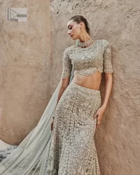 This fusion of floral embroidery is total fashion goodness for a walima outfit! A stunning teal grey organza choli embellished with intricate detailing finished with a scalloped border. The beautiful blouse is decorated with silver embellishment which is further prominent with tilla,daka, kora, Kundan and the real magic of Zardozi.  It is paired with a heavily embellished back-train lehenga with botanical motifs and geometric patterns. Its dupatta is made from a net. The dupatta is a wide embellished border that added divine charm to the entire ensemble.