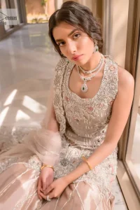 The beauty of idealism is captured with a touch of sparkle. This exclusive rose pink ensemble is beautifully translated on rose pink canvas, which makes this walima outfit stand out in the crowd. This fully embellished article comes with a short shirt lehenga style that gives it a bold look. The round neckline makes this masterpiece a unique cut. The short shirt is adorned with a silver embroidery which involves tilla, dabka, kora, Kundan and the real magic of Zardozi. Further, the sleeveless style of the following short shirt adds charm to the lehenga with heavy border embellishments on it. Carrying out its final contemporary look with a net scalloped dupatta framed with four-sided embellished borders and cross lines all over.