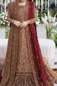 The copper long shirt is paired with a farshi-style lehenga and a maroon organza dupatta to create a traditional look. The shirt is made from pure tissue, which gives it a soft metallic finish that works well with antique embroidery spread across the front and sleeves. Its round neckline and full sleeves let the colour and craftsmanship stand out